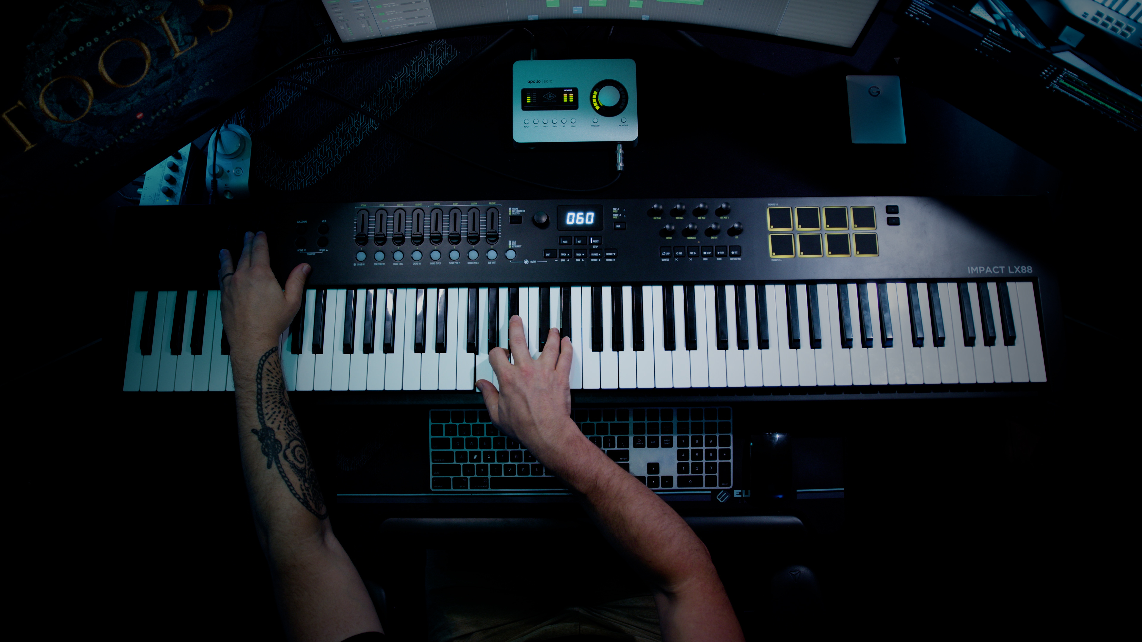 A composer at a studio console playing a weighted keyboard, Hollywood Scoring Tools open on the screen